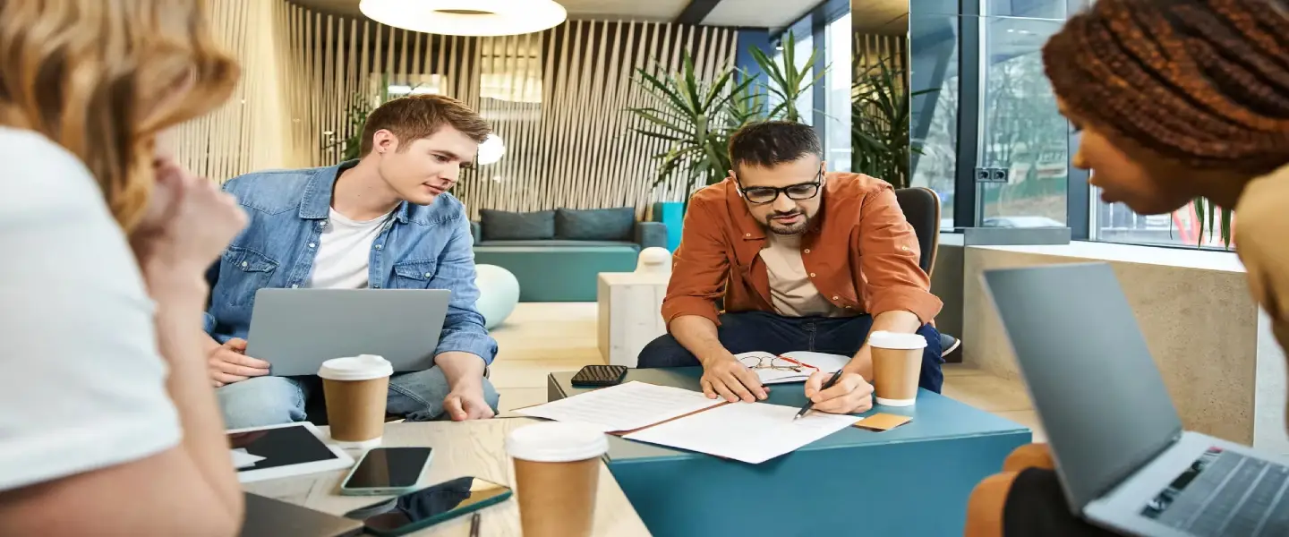 A diverse group of individuals working together around a table with laptops in a modern business setting